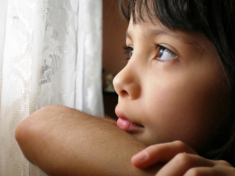 Detalle de un menor mirando a través de un visillo