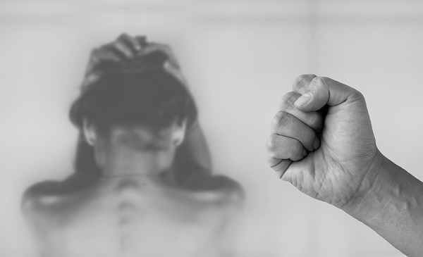 Un puño cerrado en primer plano y una mujer detrás intentando protegerse