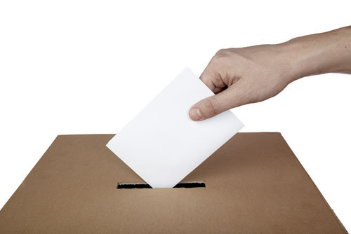 Detalle de una mano metiendo una papeleta electoral en una urna