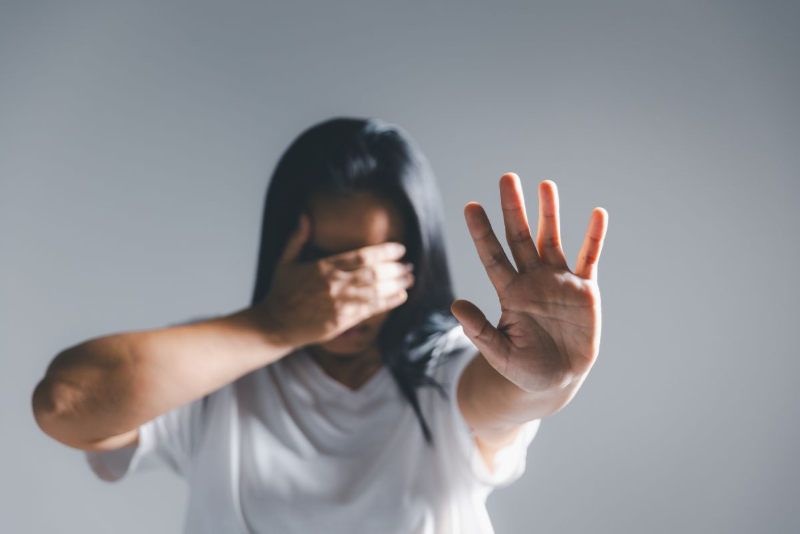 Imagen de una mujer tapándose la cara con su mano derecha mientras enseña la palma de su mano izquierda a la cámara