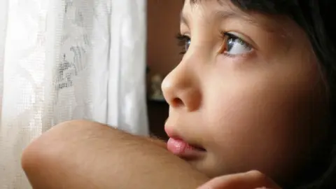 Detalle de un menor mirando a través de un visillo