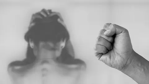 Un puño cerrado en primer plano y una mujer detrás intentando protegerse