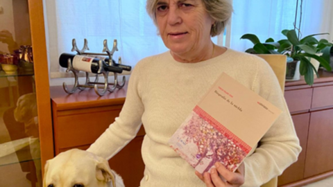 La activista Teresa Palahí con su libro en la mano y su perro guía, en su casa |Foto cedida por Palahí.