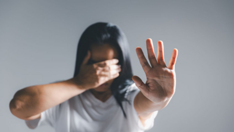 Imagen de una mujer tapándose la cara con su mano derecha mientras enseña la palma de su mano izquierda a la cámara